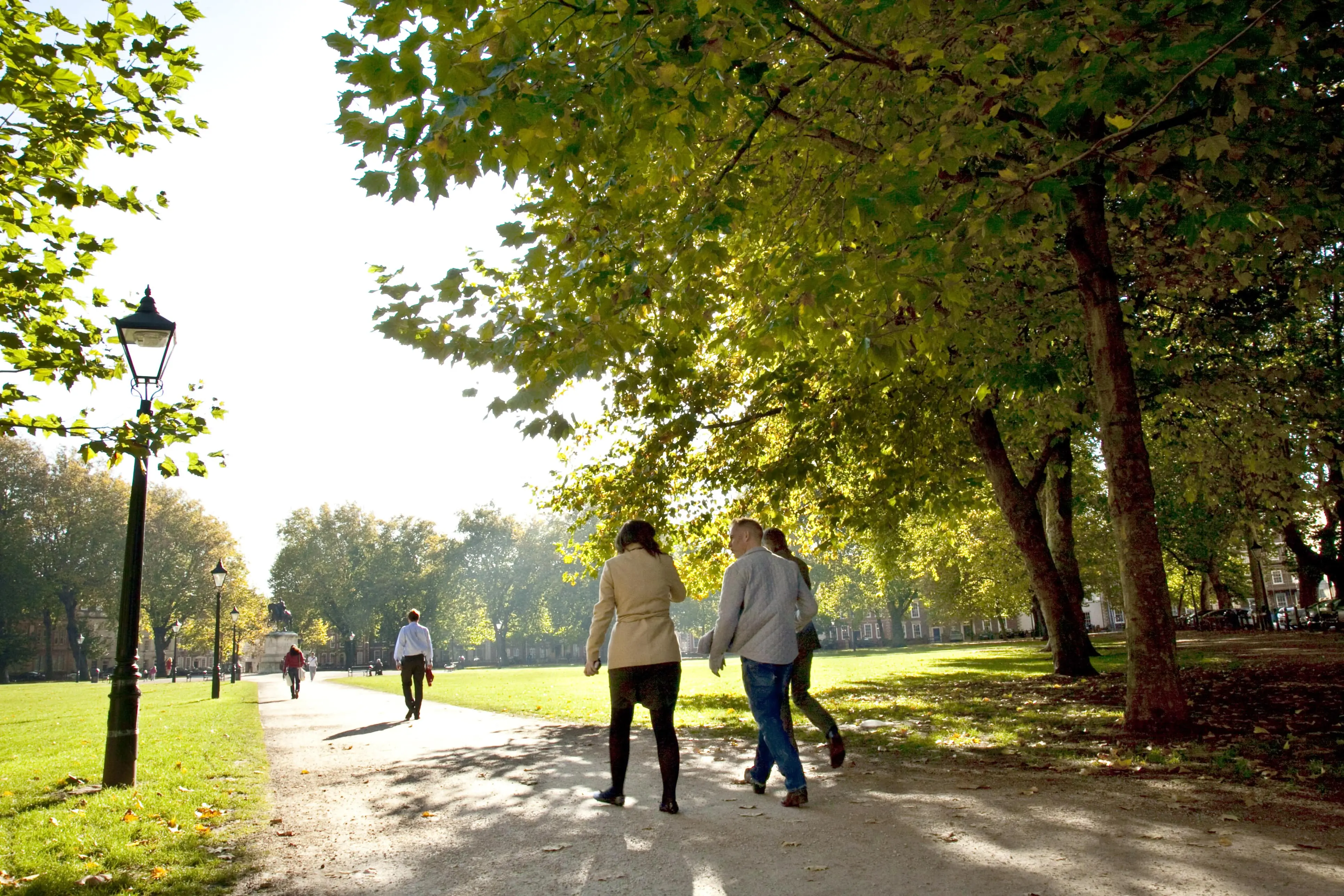 Three people walking through a leafy green park